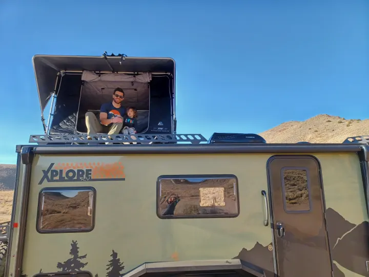 Family adventure in an Xplore RV rental! Dad & child relax in the rooftop tent, reflecting desert views.. Xplorer X22 2022