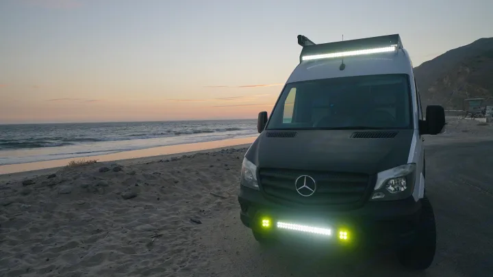 This Mercedes Sprinter RV rental shines bright on a sandy beach at sunset, perfect for coastal camping adventures.. Mercedes-Benz Sprinter 2017