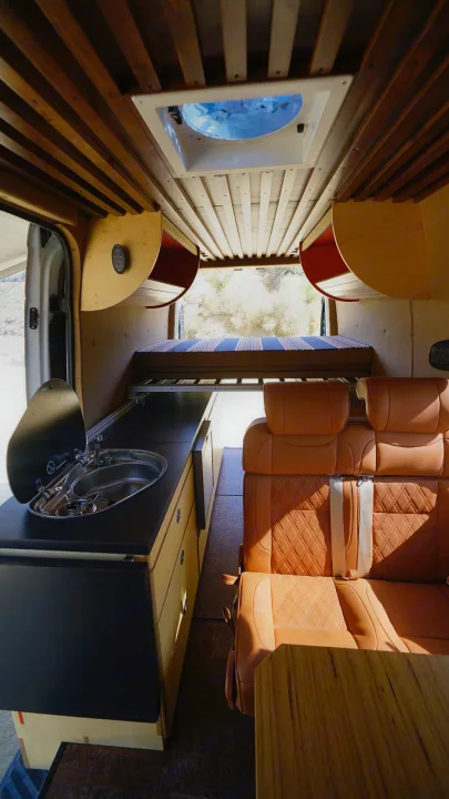 Explore this custom RV rental's warm interior: a compact kitchen with sink, luxurious quilted seating, and modern wood paneling.. Mercedes-Benz Sprinter 2017