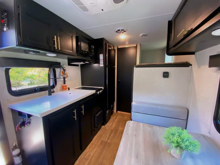 RV rental interior: modern kitchen with black cabinets, white counters, dining area, and cozy bench seating.. Forest River Wolf Pup -Black Label 2021