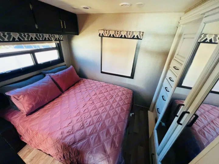 RV rental bedroom: pink quilted bed, overhead cabinets, and a mirrored wardrobe for a comfortable stay.. Jayco Alante 2021