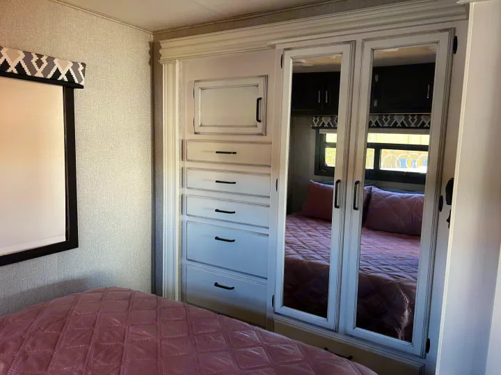 Compact RV bedroom featuring built-in storage with mirrored doors, a comfortable bed, and stylish valance. Perfect for your next RV rental adventure.. Jayco Alante 2021