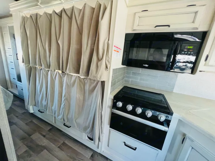 Modern rv rental interior: features a sleek kitchen with microwave, stove, and stylish privacy curtains over storage.. Jayco Alante 2021