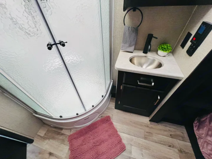 Experience comfort in this compact RV rental bathroom, featuring a curved shower, modern vanity, and cozy pink mat.. Jayco Alante 2021
