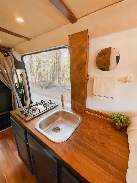 Inside this **RV rental**, a compact camper kitchen with wooden counters, sink, gas stove, and scenic forest views.. Other Dodge 2021