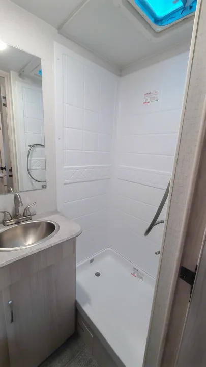 RV rental bathroom with bright white shower walls, a skylight, and a light-toned vanity with a metallic sink.. Winnebago Hike 2022