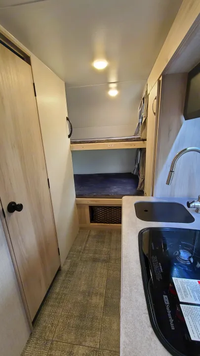 RV rental interior featuring a compact kitchen with a stovetop and sink, opposite bunk beds.. Winnebago Hike 2022