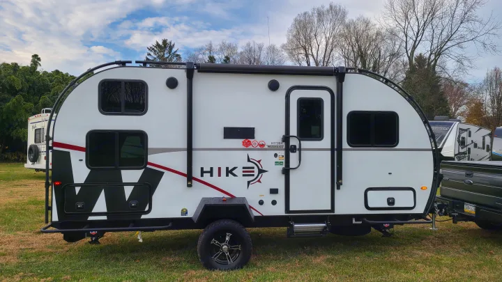 A white Winnebago Hike travel trailer, ideal for an rv rental, parked on grass & hooked to a truck.. Winnebago Hike 2022