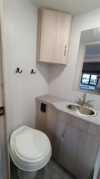 This compact RV rental bathroom features a toilet, sink vanity, overhead cabinet, and hooks for convenience.. Winnebago Hike 2022