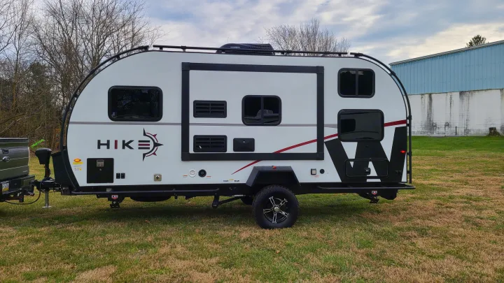 This RV rental is a rugged, white and black off-road travel trailer parked on a grassy field, ready for adventure.. Winnebago Hike 2022