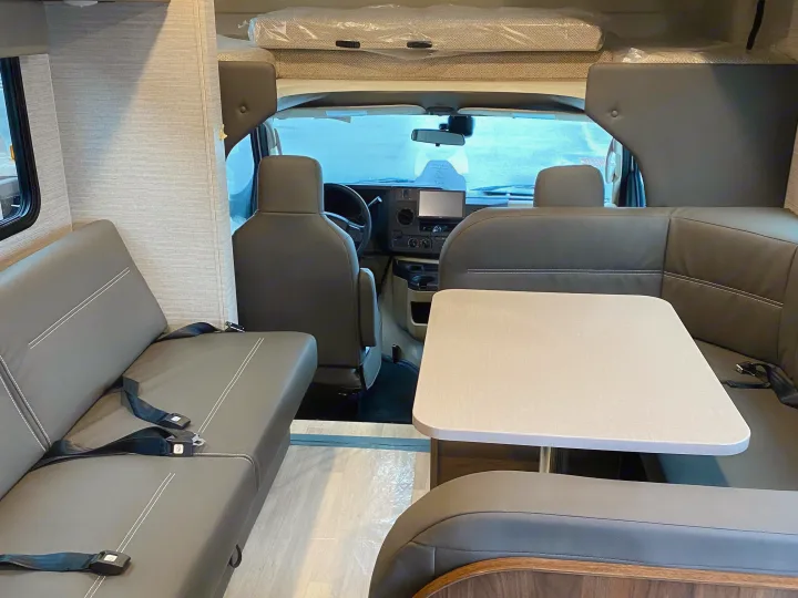 Inside this RV rental: comfortable dinette seating & forward view of the cockpit and overhead bunk. Perfect for road trips.. Winnebago Minnie Winnie 2021