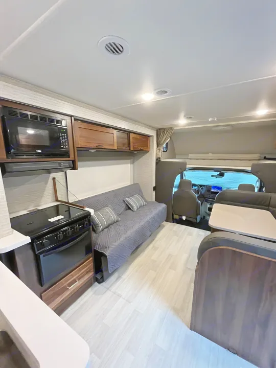 Clean & modern RV rental interior featuring kitchen, living space, dining area, and overhead bunk.. Winnebago Minnie Winnie 2021