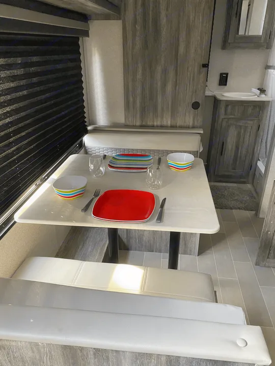 Interior view of an RV rental: dining table set for two with colorful dishes, next to a small bathroom.. Forest River Salem FSX 2021