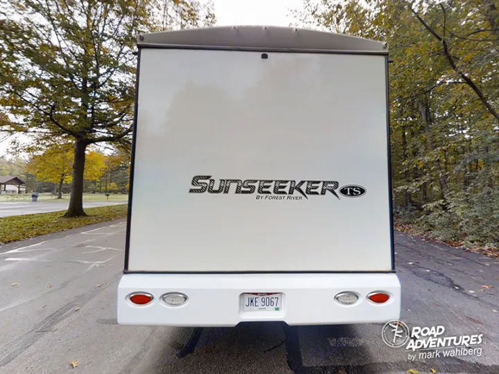 RV rental adventures await! Rear of a white Sunseeker RV parked in a park with autumn trees.. Forest River Sunseeker 2022