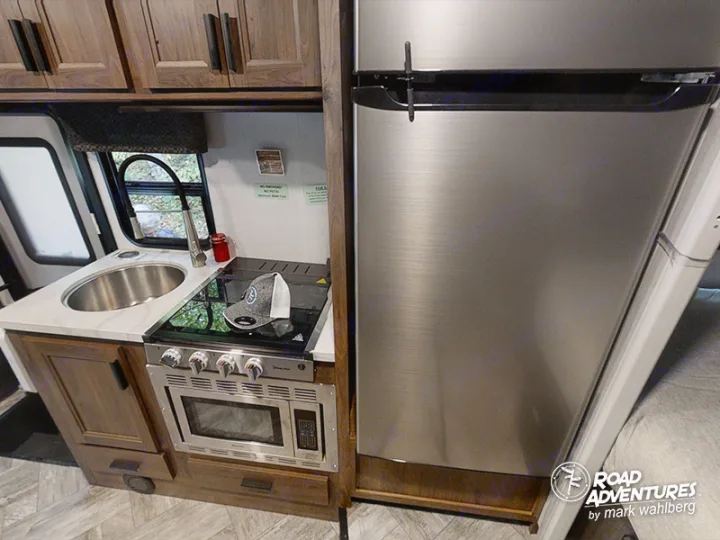 Compact RV rental kitchen: stainless steel fridge, microwave, sink, and stove. Perfect for mobile living.. Forest River Sunseeker 2022