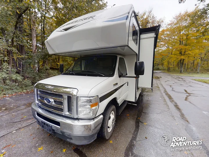 White Ford Seeker Class C RV rental, with a slide-out, parked on a wet road in an autumn forest. Ready for adventures.. Forest River Sunseeker 2022