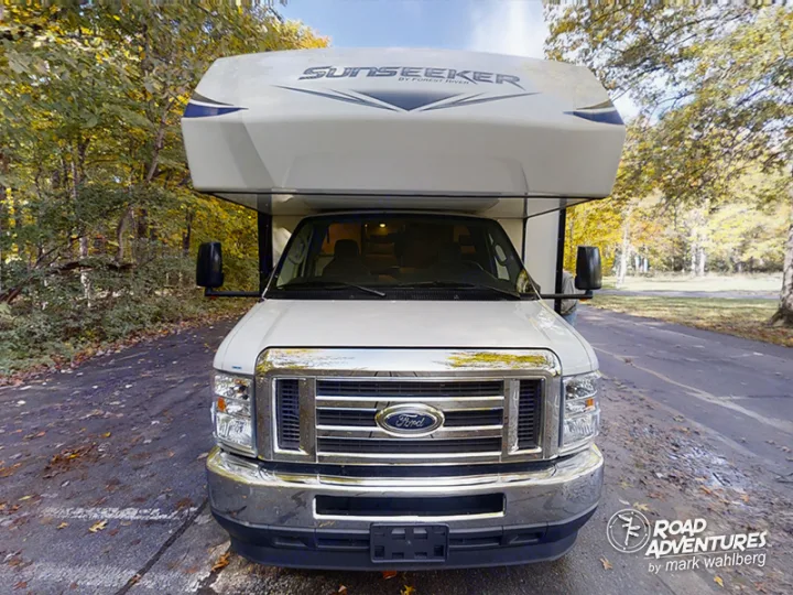 This white Ford Sunseeker Class C RV rental is parked on an asphalt road, surrounded by autumn trees, ready for adventure.. Forest River Sunseeker 2021