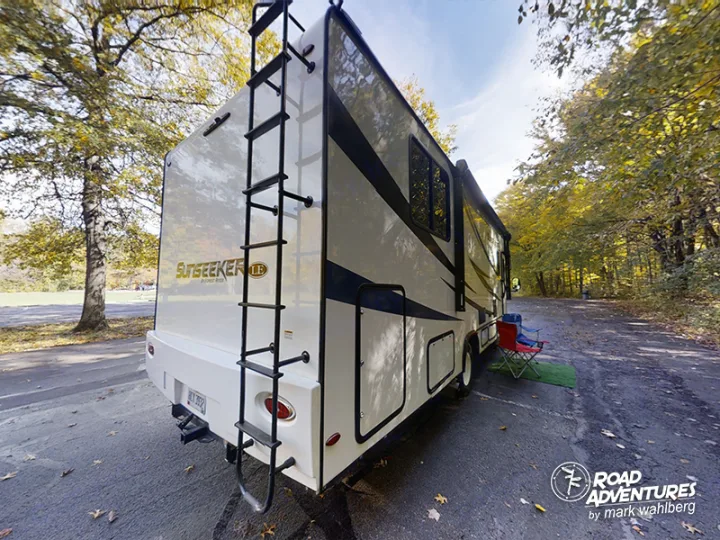 Sunseeker RV rental, a white motorhome, parked in an autumn forest campsite with chairs.. Forest River Sunseeker 2021