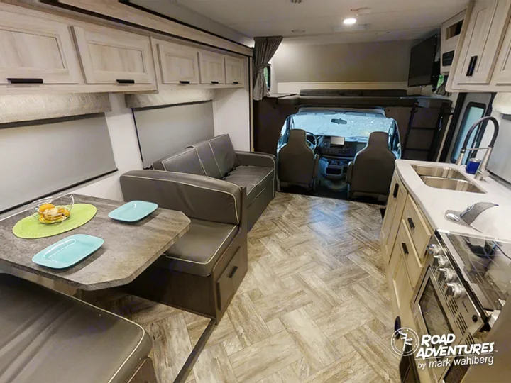 Bright RV rental interior: kitchen with sink, dinette with light blue plates, sofa, and driver's cabin for travel comfort.. Forest River Sunseeker 2022