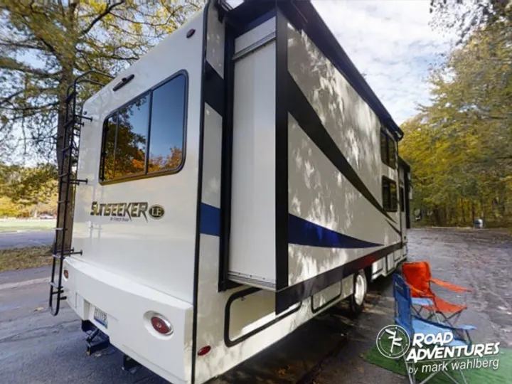 White Sunseeker RV rental parked at a wooded campsite with chairs. Perfect for a memorable road trip.. Forest River Sunseeker 2022