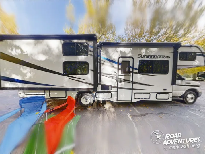 Large white Sunseeker RV rental extended for camping comfort, with blue and red chairs set up outside.. Forest River Sunseeker 2022