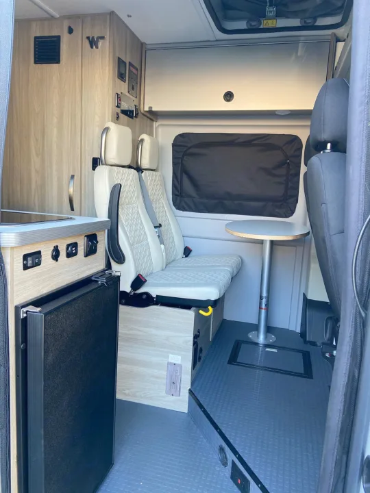 RV rental: Interior view of a modern camper van, featuring light seating, compact kitchenette with fridge, and a table.. Winnebago Solis 2021