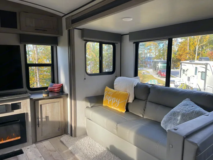 Bright RV rental living space featuring a gray couch, cozy decor, and a scenic lake and campground view outside.. Keystone RV Springdale 2021