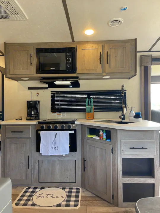 Modern RV rental kitchen featuring a microwave, stove, sink, and coffee maker.. Keystone RV Springdale 2021