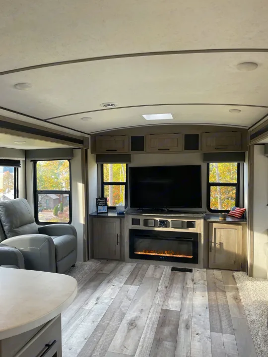 Comfortable RV rental living space with modern light flooring, recliners, TV, and an inviting electric fireplace.. Keystone RV Springdale 2021