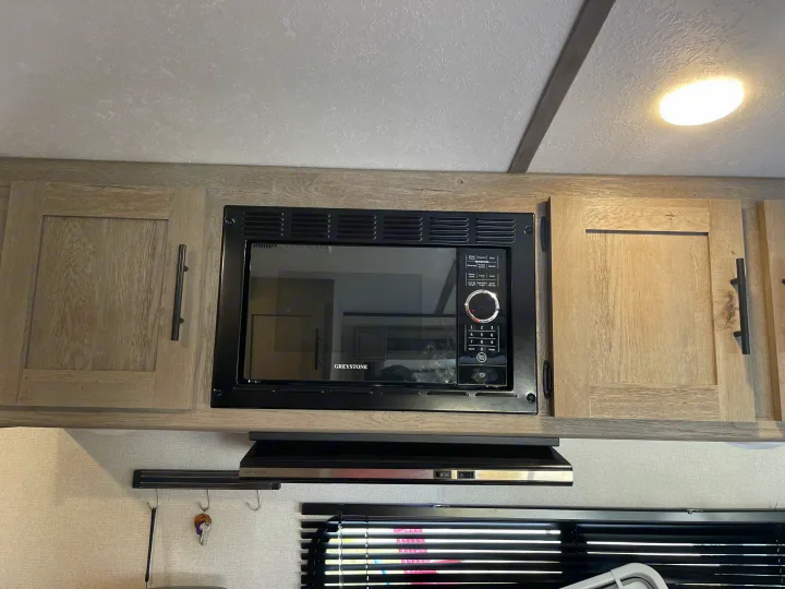 GREYSTONE microwave and range hood in an RV rental kitchen, showing compact appliances and wood-grain cabinets.. Keystone RV Springdale 2021