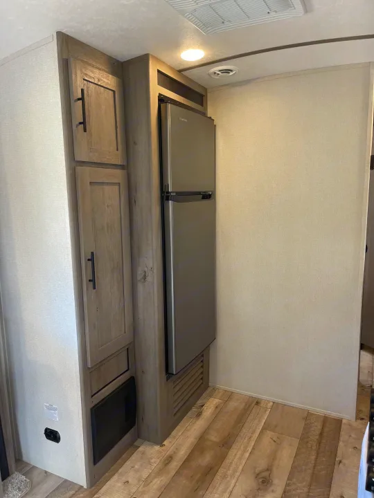 An RV rental interior with light wood cabinetry, a stainless steel refrigerator, and wood-look flooring for efficient use of space.. Keystone RV Springdale 2021