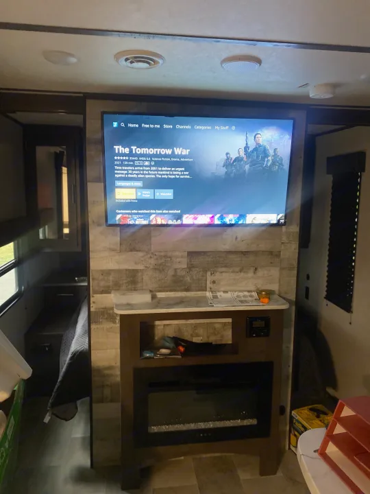 An RV rental interior featuring a TV playing "The Tomorrow War" above an electric fireplace, creating a cozy living space.. Coleman Lantern 2021