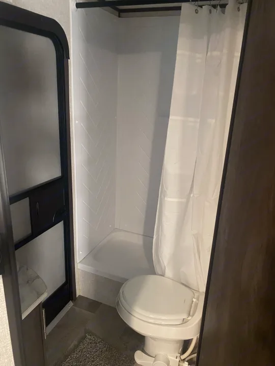 RV rental: A compact RV bathroom featuring a white shower stall with herringbone walls, shower curtain, and toilet.. Coleman Lantern 2021