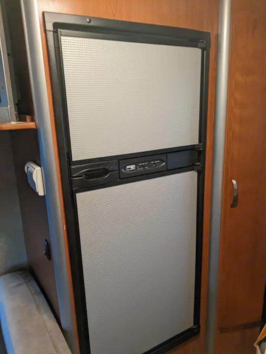 Compact RV rental refrigerator with textured gray doors and a control panel, integrated into wood cabinetry.. Winnebago Itasca Navion 2008