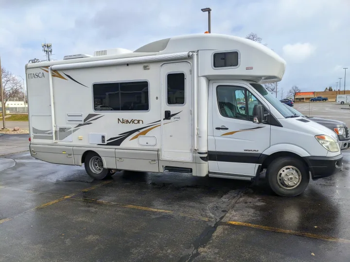 This white Itasca Navion motorhome, a type of RV rental, is parked in a wet lot. It's built on a Mercedes-Benz Sprinter chassis.. Winnebago Itasca Navion 2008