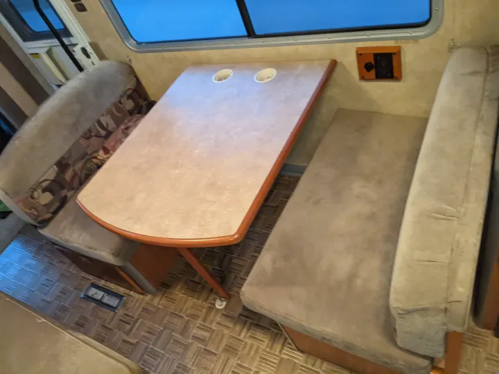 Cozy RV rental dinette featuring cushioned benches, a table with cup holders, and an expansive window view.. Winnebago Itasca Navion 2008