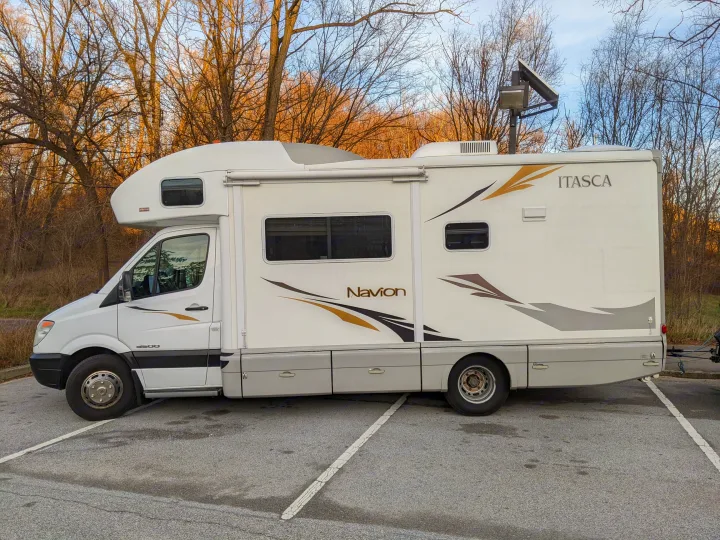 A white Itasca Navion Class C RV with rooftop solar & antenna, ideal for an rv rental adventure, parked on asphalt.. Winnebago Itasca Navion 2008