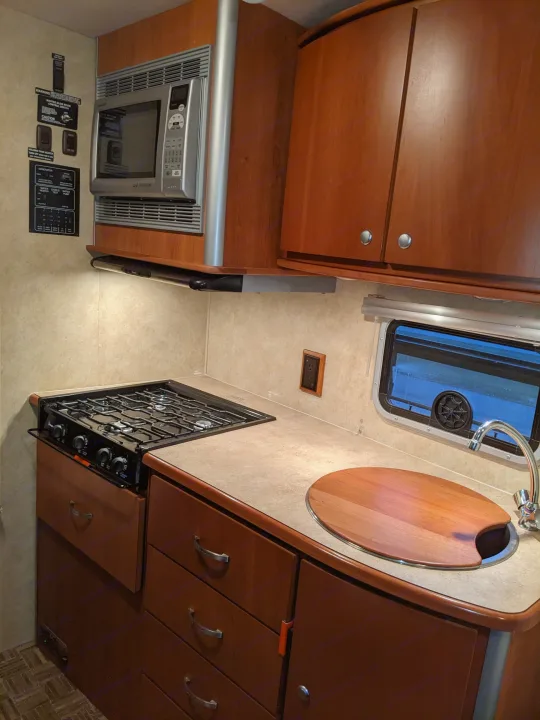 RV rental kitchen: gas stove, microwave, sink, and control panel. Functional space for travel.. Winnebago Itasca Navion 2008