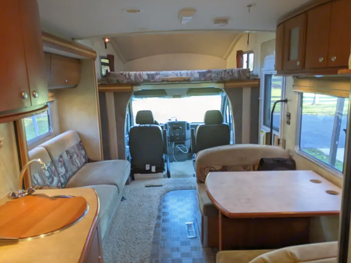Spacious RV rental interior featuring a cockpit, overhead bunk, kitchen, and dinette for comfortable travel.. Winnebago Itasca Navion 2008