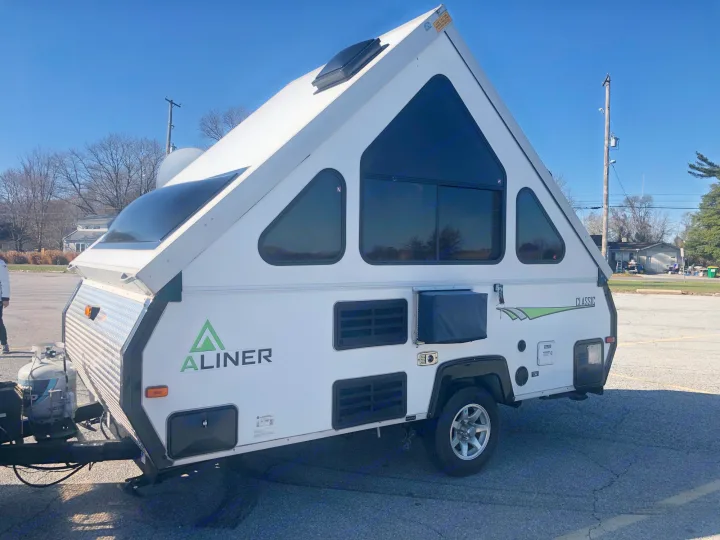 A white A-Liner A-frame travel trailer, a great option for an RV rental, sits on asphalt under a clear sky.. A Liner A Liner Popup Trailer 2014