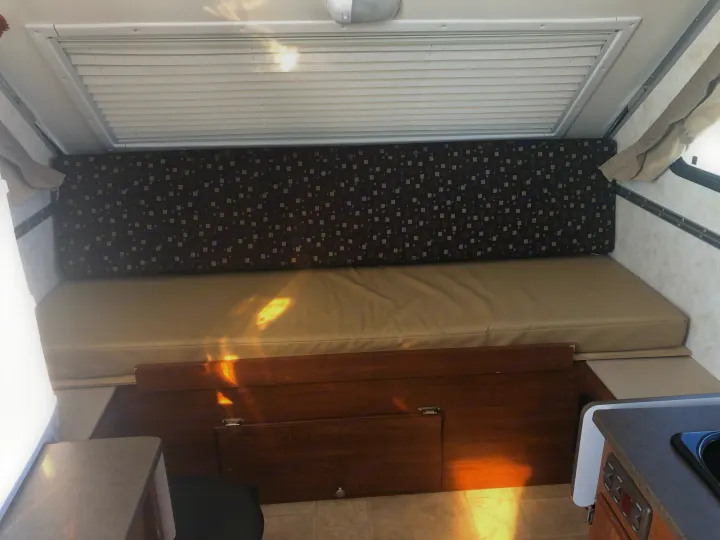 Cozy RV rental interior featuring a bed, wooden storage, and a compact kitchen counter with sink.. A Liner A Liner Popup Trailer 2014