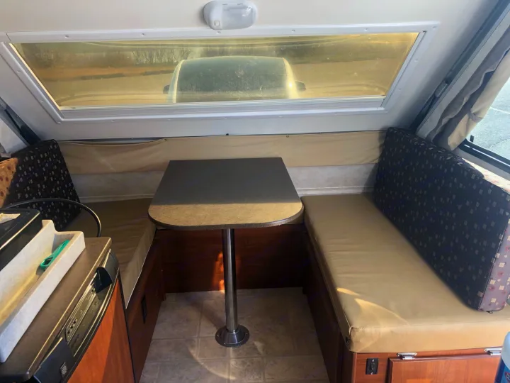 Inside an RV rental, featuring a cozy dining area with table, benches, and a large window showing a car outside.. A Liner A Liner Popup Trailer 2014