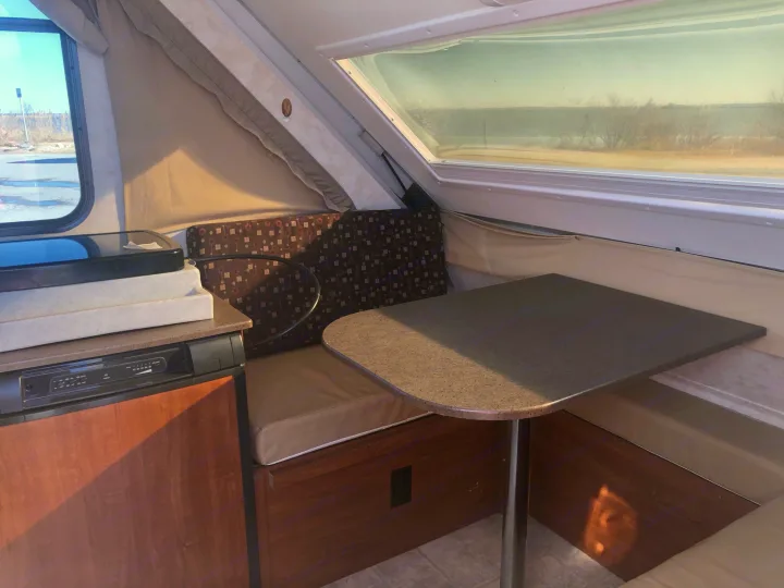 Inside an RV rental: a compact A-frame camper featuring a bright dinette area, large windows, and a built-in fridge.. A Liner A Liner Popup Trailer 2014