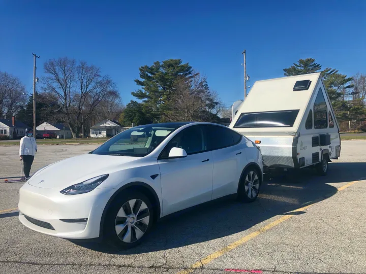 White Tesla Model Y towing an A-liner RV, ideal for an RV rental. Person nearby, highlighting modern EV towing.. A Liner A Liner Popup Trailer 2014