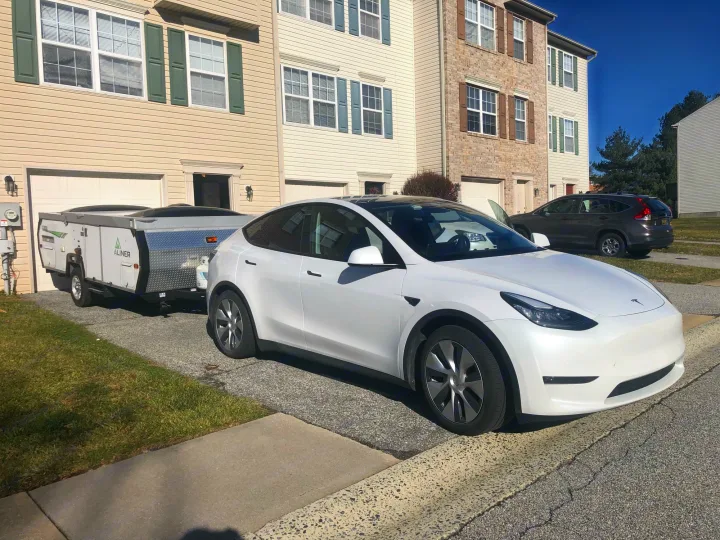 White Tesla Model Y towing a compact A-liner pop-up camper in a driveway, suitable for an RV rental adventure.. A Liner A Liner Popup Trailer 2014