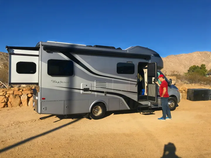 Man by an RV rental: a gray Tiffin Wayfarer motorhome with extended slide-out, parked in a desert landscape.. Wayfarer Wayfarer Motorhome 2020