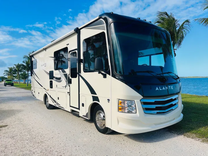 Stunning cream and black Alante Jayco RV rental parked by the ocean with palm trees under a bright blue sky. Great for travel.. Jayco Alante 2021