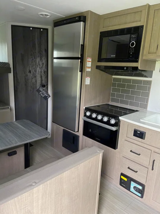 RV rental kitchen & dining area with modern appliances including fridge, microwave, stove, and a fun "Shitter's Full" sign.. Keystone Hideout 2021