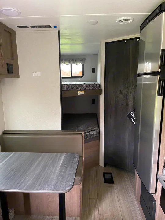 Explore this rv rental interior, featuring a cozy dining area, convenient bunk beds, and a modern stainless steel refrigerator.. Keystone Hideout 2021