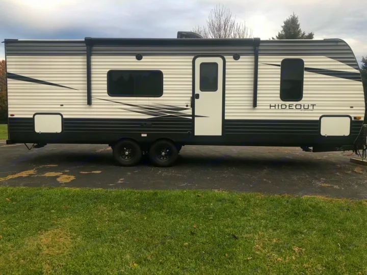 Exterior side view of a modern white and black Keystone Hideout RV rental travel trailer parked on pavement.. Keystone Hideout 2021